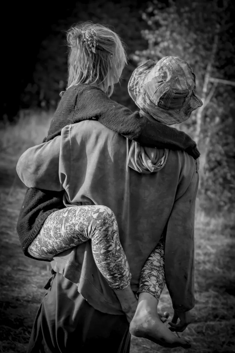 Child being carried piggyback along a wooded path in black and white